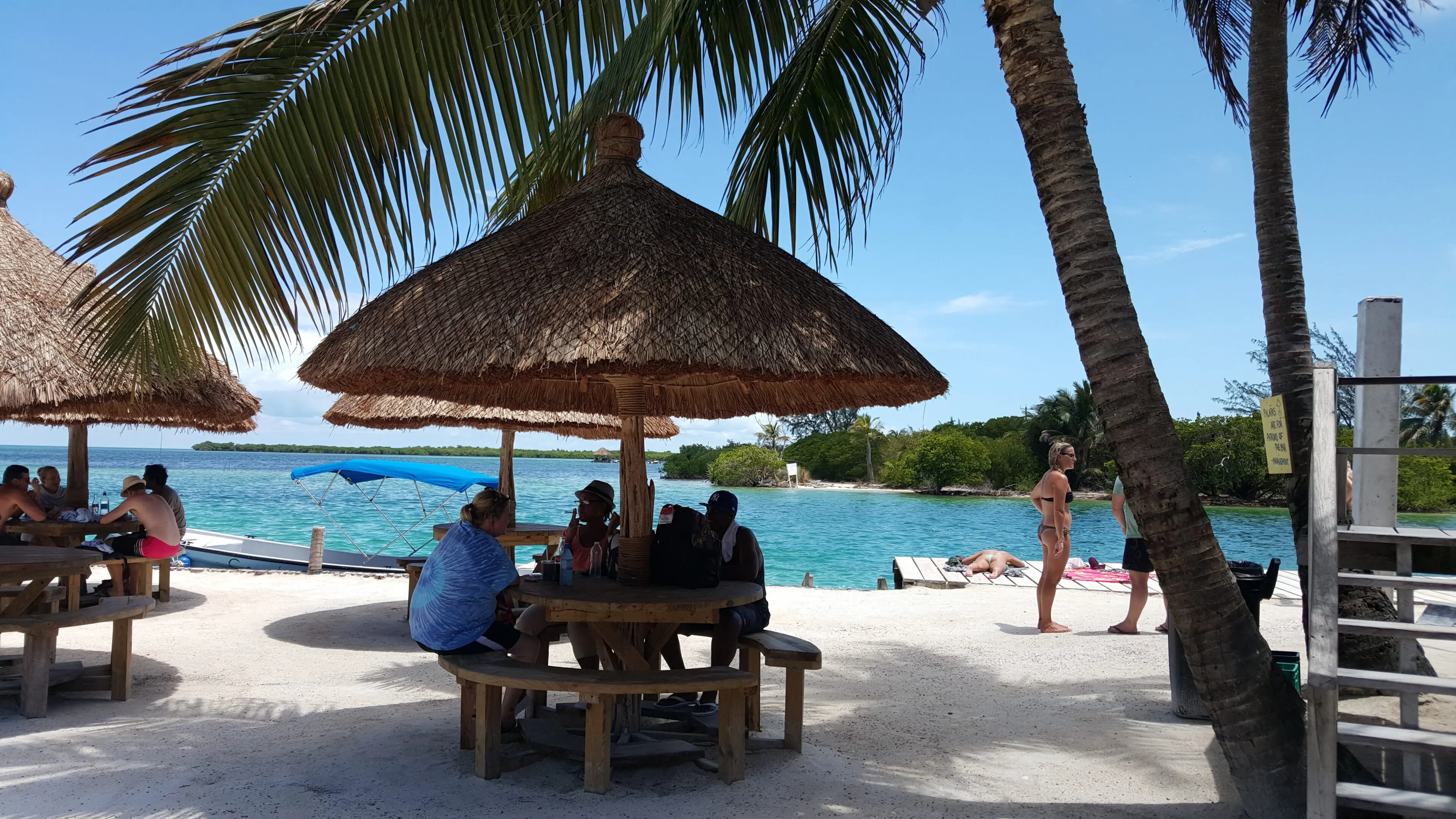 A group of people sitting at an outdoor table under a thatch umbrella.