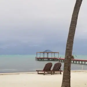 Two lounge chairs on the beach near a pier.