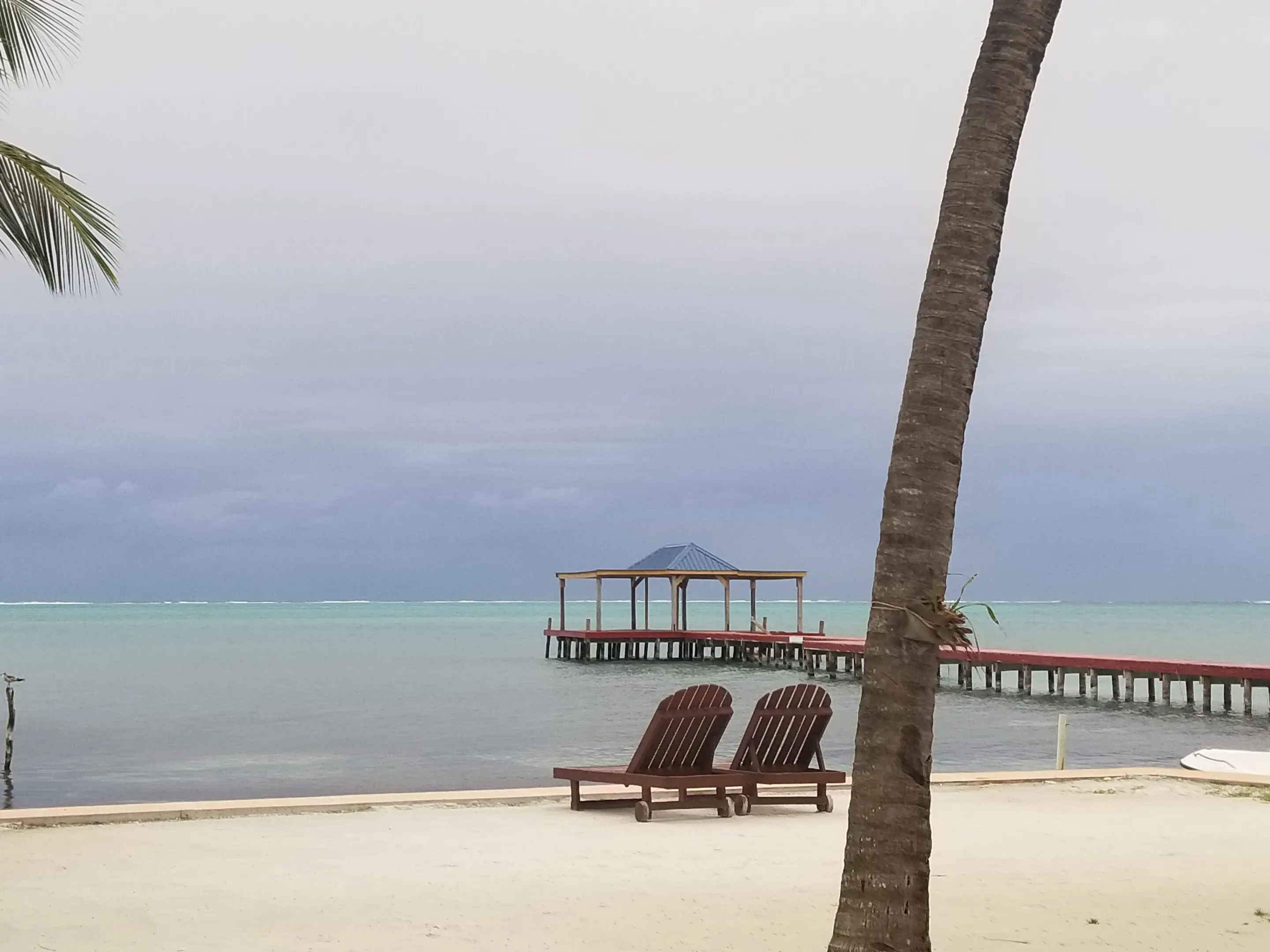 Two lounge chairs on the beach near a pier.