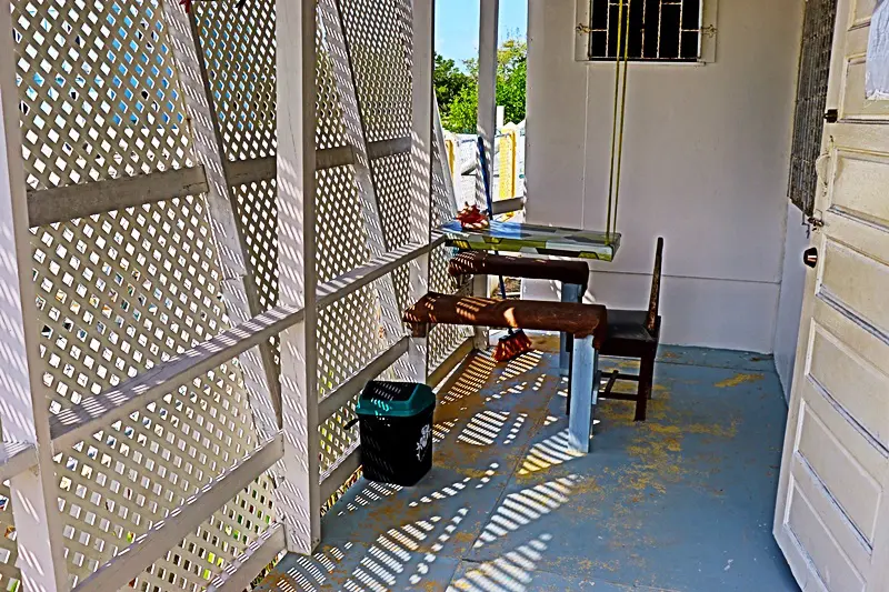 A table and chair in the sun on a porch.