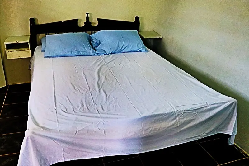 A bed with white sheets and blue pillows.