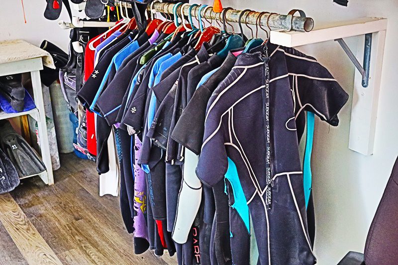 A row of wetsuits hanging on the wall.