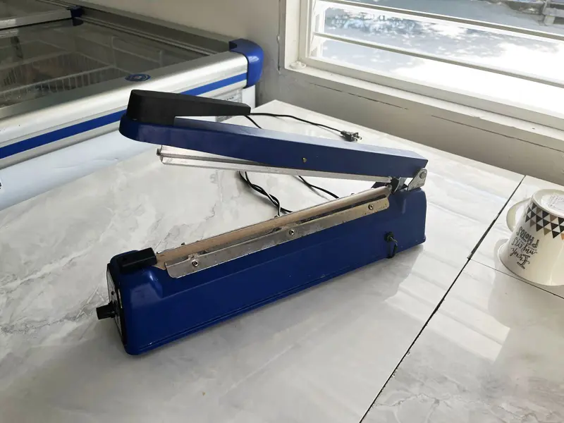 A blue and black plastic bag sealer on the floor