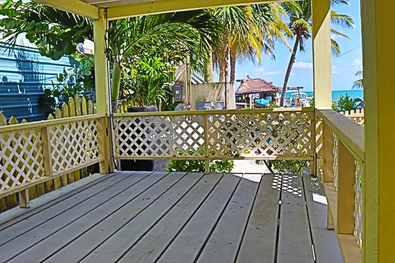 A porch with a bench and palm trees in the background.