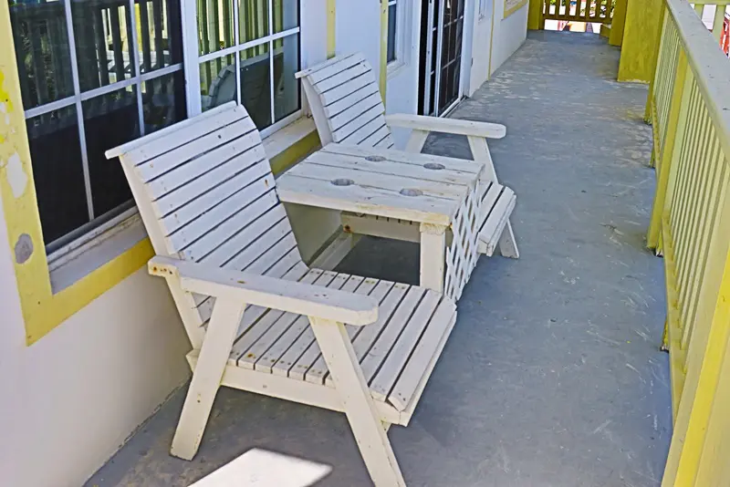 A white bench and two chairs on the porch.