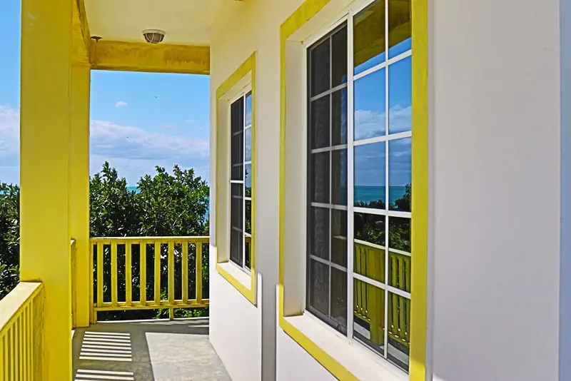 A porch with yellow trim and windows overlooking the ocean.