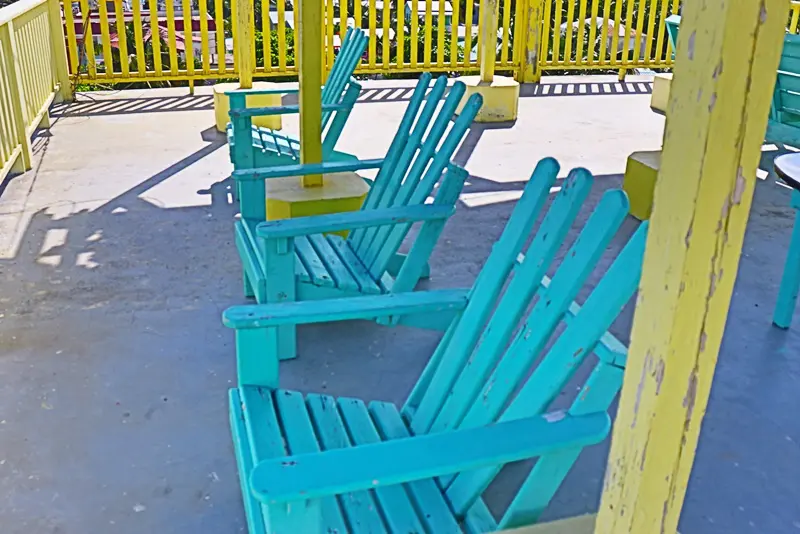 A row of blue lawn chairs sitting next to an umbrella.