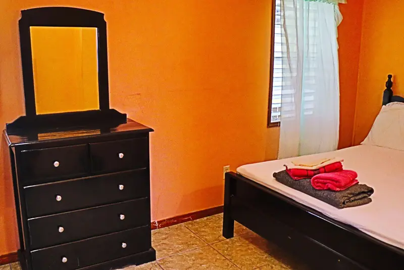 A bedroom with an orange wall and black dresser.