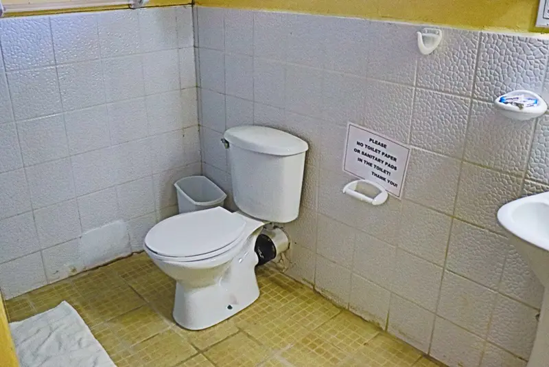 A toilet in the corner of a bathroom with a sign on it.