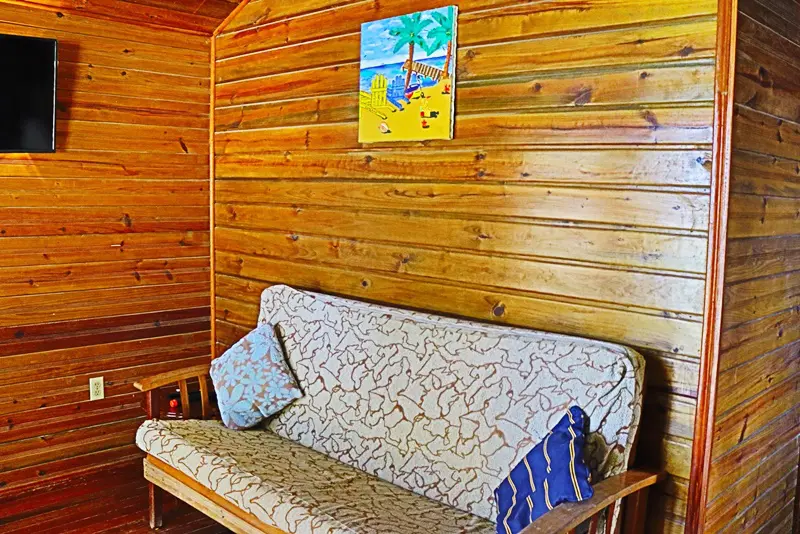 A couch in the corner of a room with wooden walls.