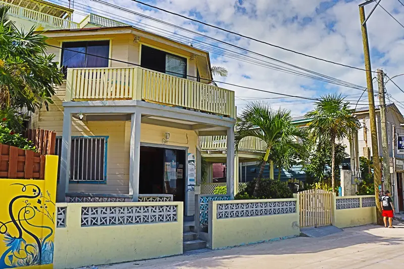 A yellow house with a balcony and palm trees.