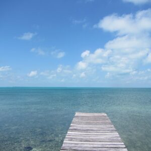 A dock in the middle of an ocean under a blue sky.