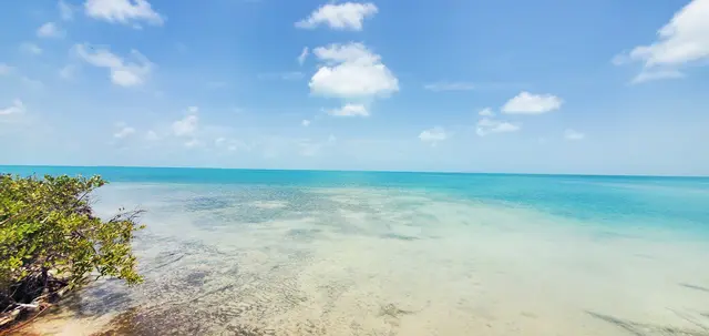 A beach with blue water and white clouds in the sky.