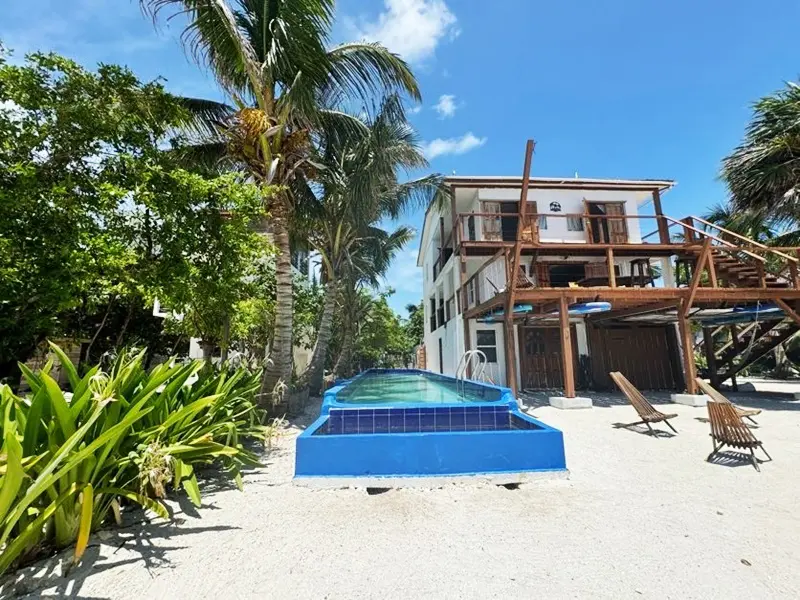 A pool on the beach with a house in the background.