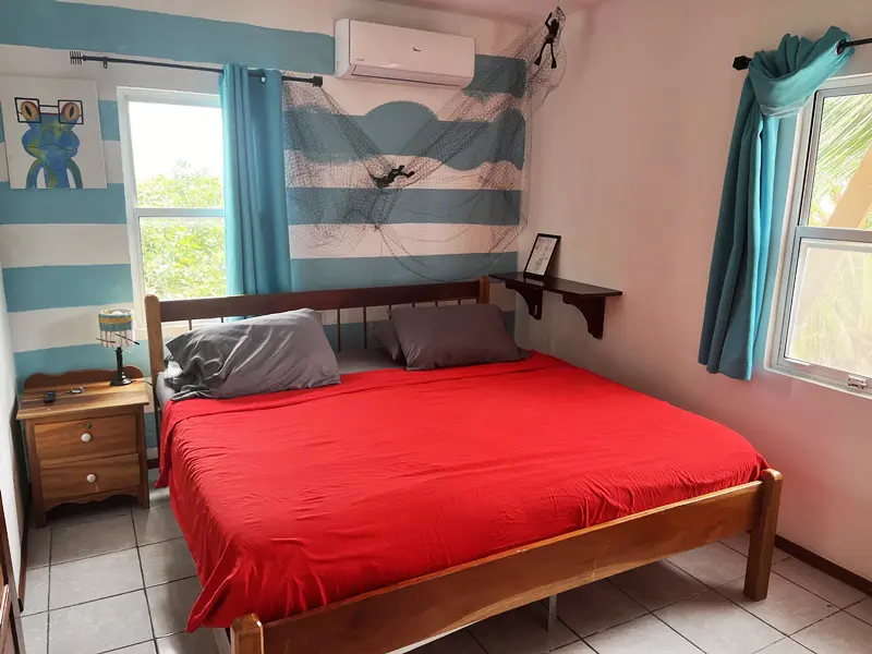 A bed room with a red bedspread and blue curtains